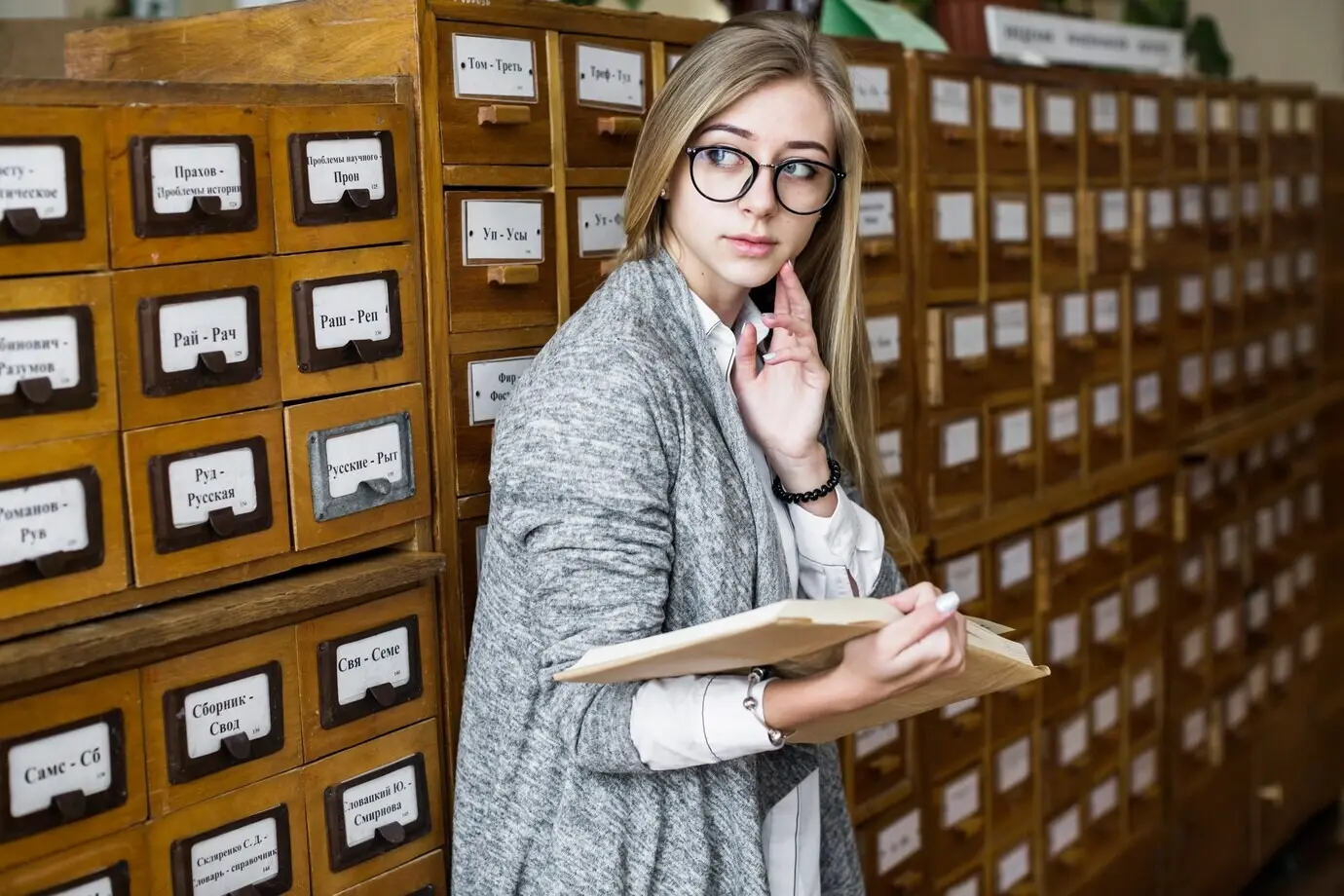 Женщина рядом с библиотечным каталогом, смотрит в сторону.